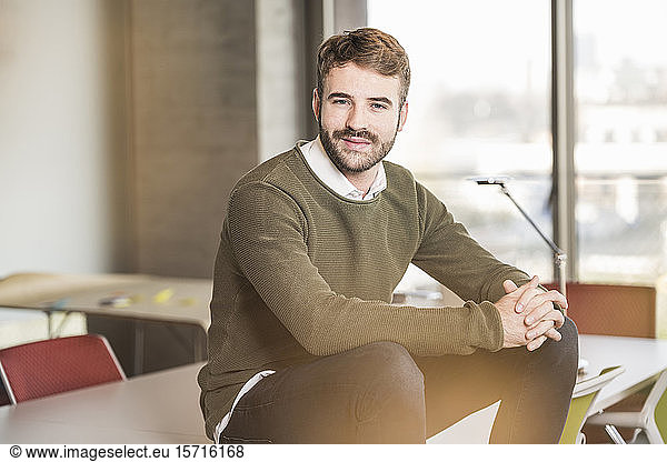 Portrait of a confident young businessman sitting on conference table in office