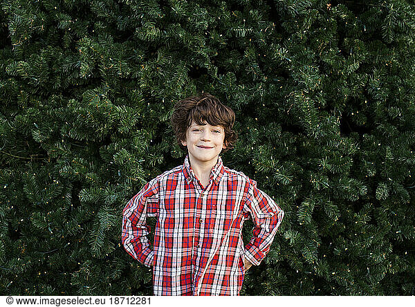 portrait of a confident young child smiling in front of lit pine tree