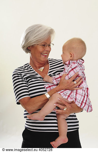 Portrait of a congenial woman  60 years old  senior citizen  with grey hair  holding her grand-daughter in her arms