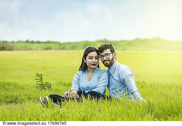 Portrait of a couple in love sitting on the grass in the field  Romantic couple sitting on the grass looking at the camera  Two lovers sitting on the grass looking at the camera