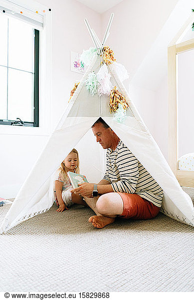 Portrait of a father and daughter reading together in a play tipi