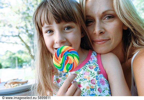 Portrait of a girl holding a lollipop with her mother and smirking