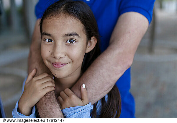 Portrait of a girl standing with her dad's arms wrapped around her in an embrace; Hong Kong  China