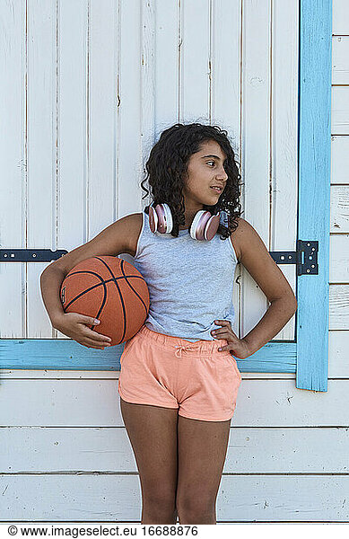 Portrait of a girl with curly hair with a basketball and headphones