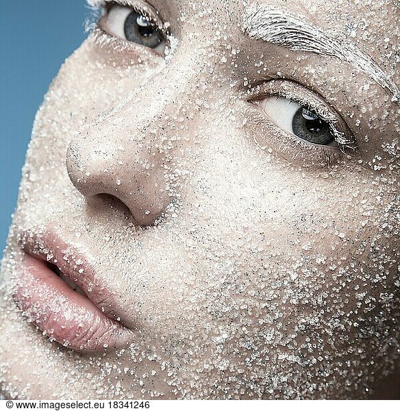 Portrait of a girl with pale skin and sugar snow on her face. Creative art beauty fashion. Picture taken in the studio on a blue background