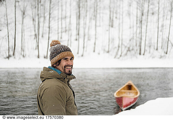 Portrait of a happy man next to a canoe on the snowy river.