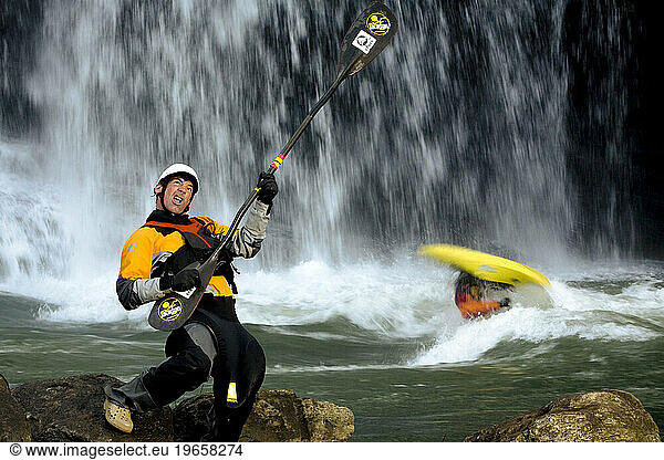 Portrait of a male kayaker playing air guitar in front of a waterfall..