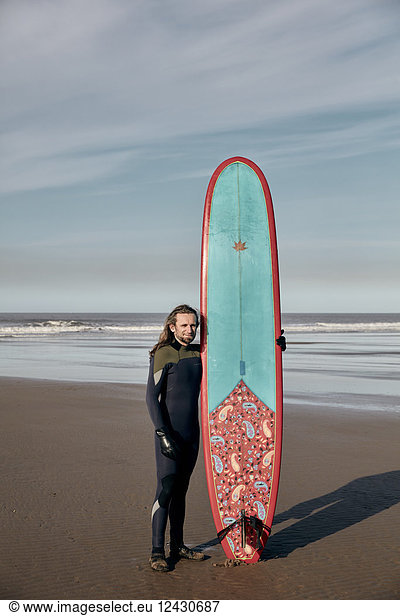Portrait of a man holding a decorated surf board on a sandy beach