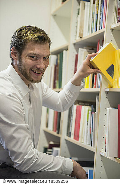 Portrait of a mid adult businessman choosing books from bookshelf in an office  Bavaria  Germany
