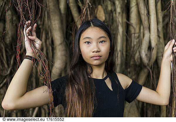 Portrait of a preteen girl standing among vines and tree roots; Hong Kong  China
