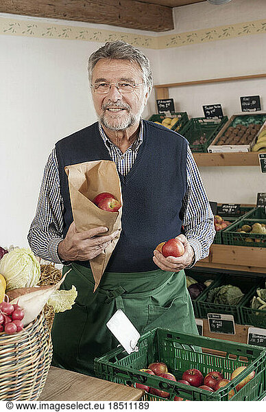 Portrait of a senior shopkeeper selling apples in the store  Bavaria  Germany