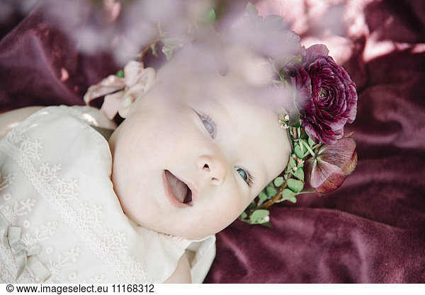 Portrait of a smiling baby girl with a flower wreath on her head.