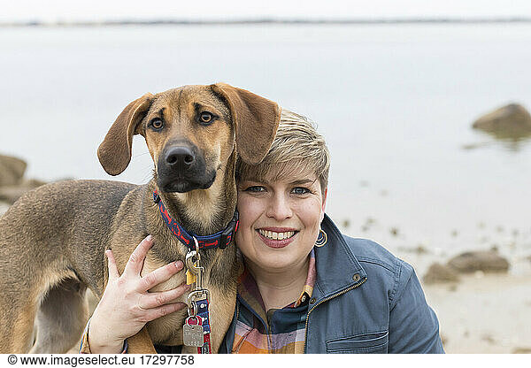 Portrait of a smiling short-haired woman with her brown puppy at beach