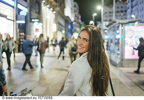 Portrait of a smiling woman walking down shopping street at night