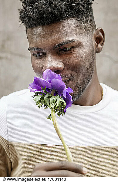 Portrait of a smiling young African American man smelling a purple flower on a brown background