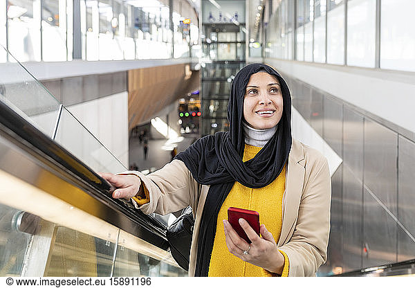 Portrait of a smiling young woman wearing hijab standing on escalator