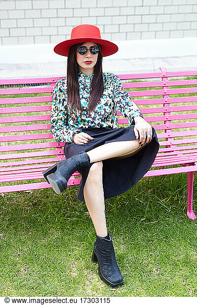 Portrait of a stylish young hispanic woman sitting on a pink bench