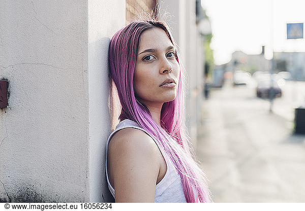 Portrait of a stylish young woman with pink hair leaning against a wall in the city