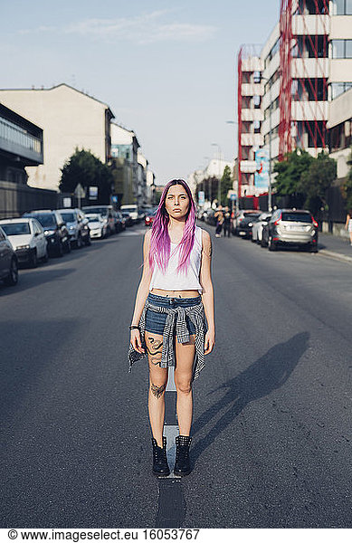 Portrait of a stylish young woman with pink hair standing on the street in the city