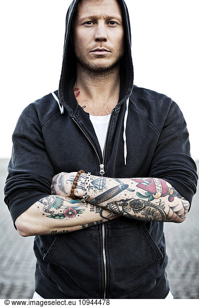 Portrait of a tattooed man in hooded jacket with arms crossed