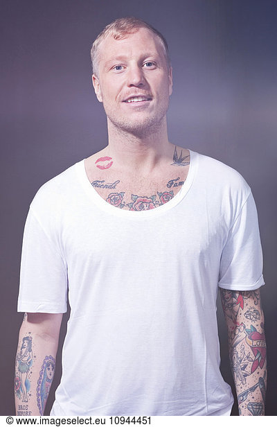Portrait of a tattooed man in t-shirt standing against purple background
