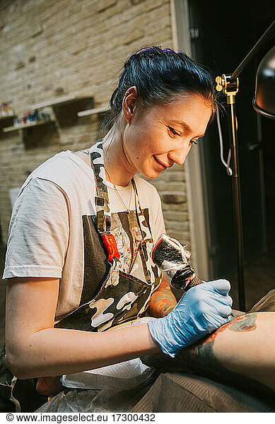 Portrait of a woman tattoo master showing a process of creation tattoo on a hand under the lamp light.