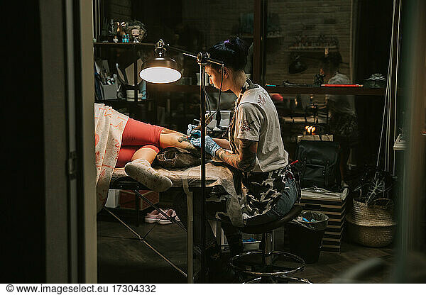 Portrait of a woman tattoo master showing a process of creation tattoo on a hand under the lamp light.
