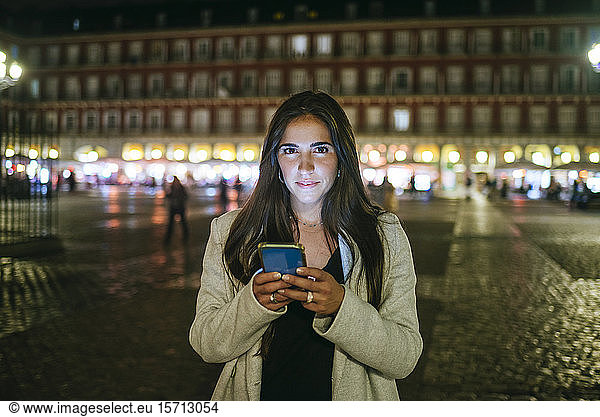 Portrait of a woman using her smartphone on Plaza Mayor at night  Madrid  Spain