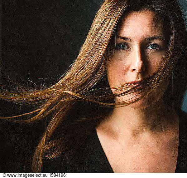 Portrait of a woman with long brown hair blowing across her face.
