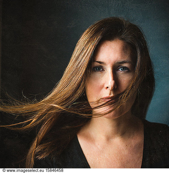 Portrait of a woman with long brown hair blowing across her face.