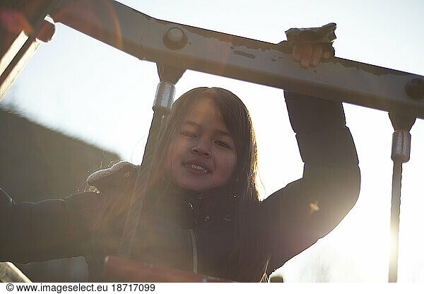 Portrait of a young Asian girl climbing in a climbing frame at school