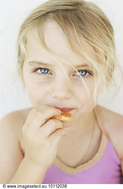 Portrait of a young blond girl  eating a mandarin  looking at the camera.
