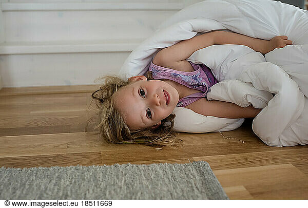 portrait of a young blond girl playing in a duvet on the floor at home