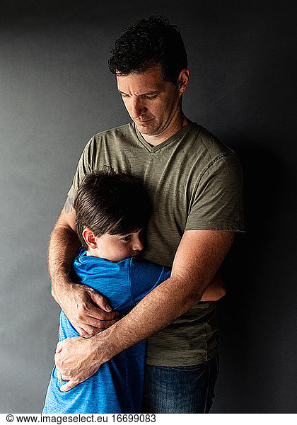 Portrait of a young boy hugging his father against a black backdrop.