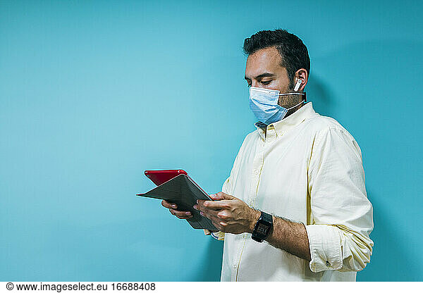portrait of a young businessman with a mask using a tablet and h