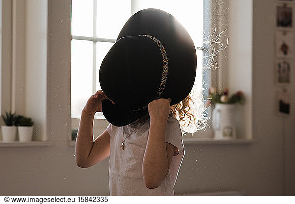 portrait of a young girl playing with a hat covering her face