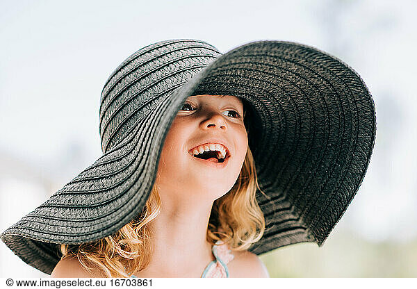 portrait of a young girl smiling outside with a large sun hat on