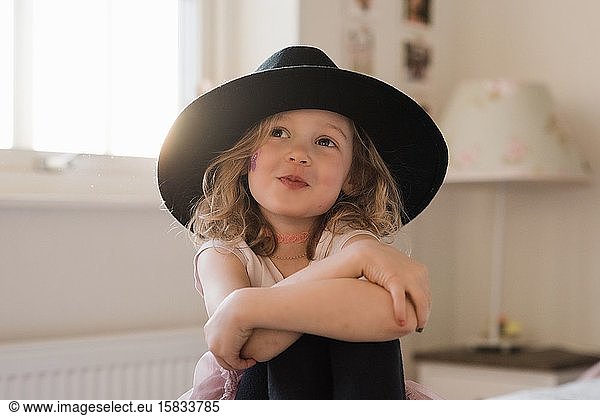 portrait of a young girl smiling with jewellery and a hat at home