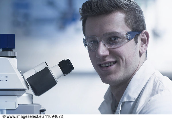 Portrait of a young male scientist using microscope in an optical laboratory