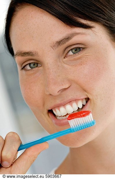 Portrait of a young woman brushing her teeth and smiling