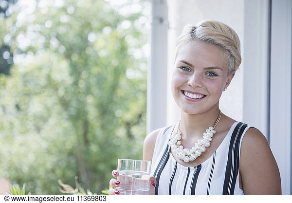 Portrait of a young woman drinking water on the balcony and smiling