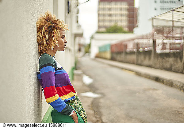 Portrait of a young woman in an afro hairstyle leaning on a wall in the city