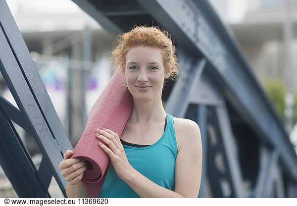 Portrait of a young woman standing with exercise mat in urban city