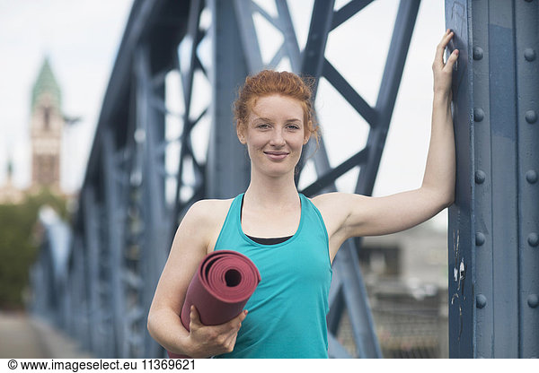 Portrait of a young woman standing with exercise mat in urban city