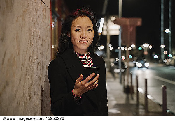 Portrait of a young woman using smartphone in the city at night  Frankfurt  Germany