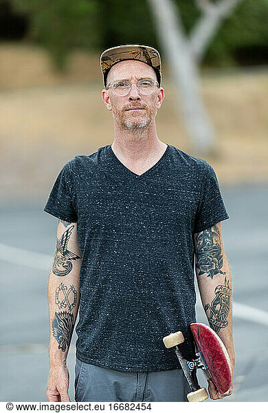 Portrait of adult male standing holding skateboard looking at camera