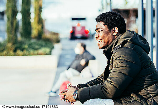 Portrait of an African American boy smiling. Sitting on a bench in an urban space.
