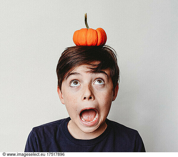 Portrait of an excited boy balancing a small pumpkin on his head.