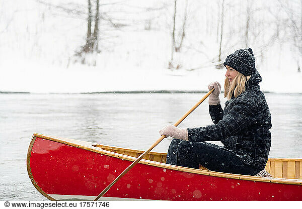 Portrait of an excited woman rowing a canoe on a snowy river.