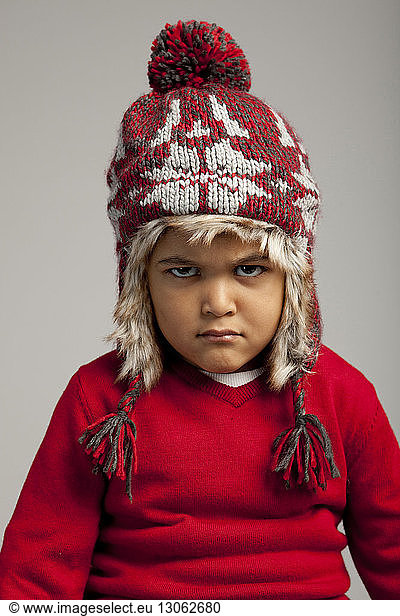 Portrait of angry boy wearing knit hat against gray background